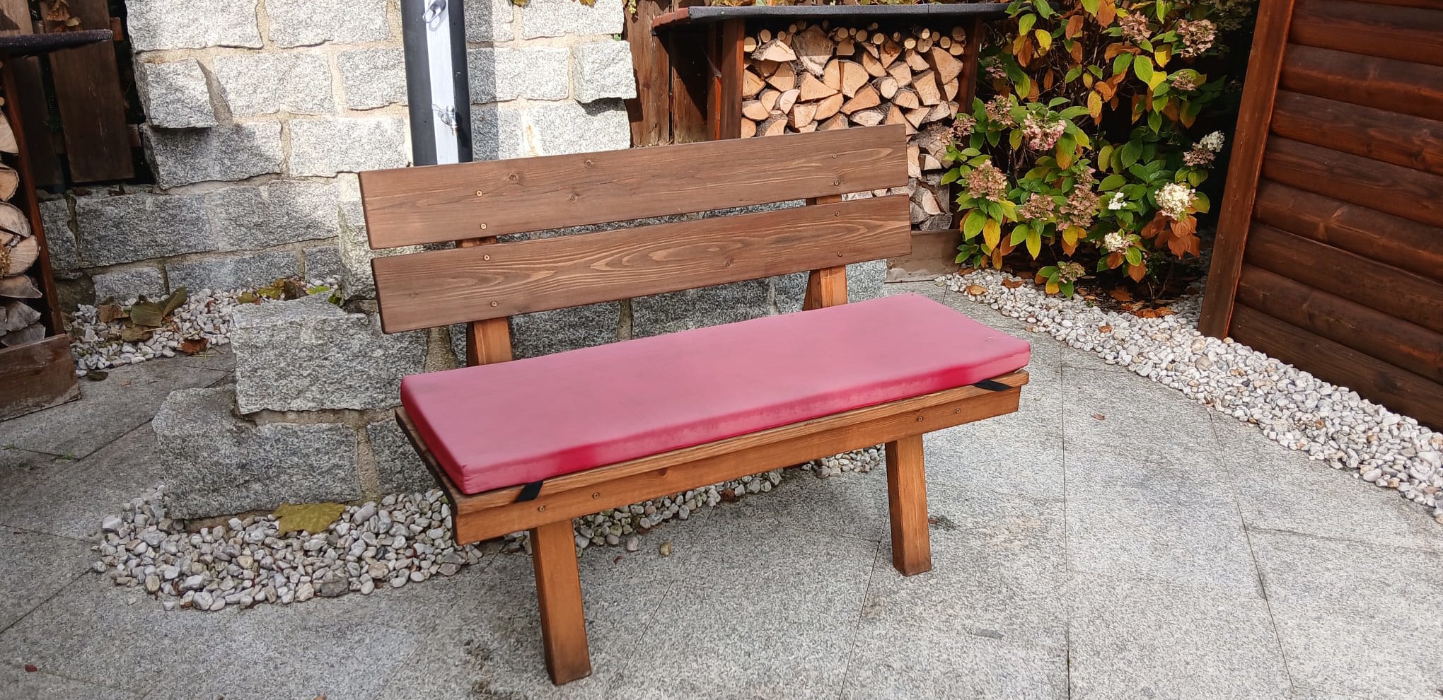 kleine Bank mit rotem Sitzkissen vor Steinmauer stehend