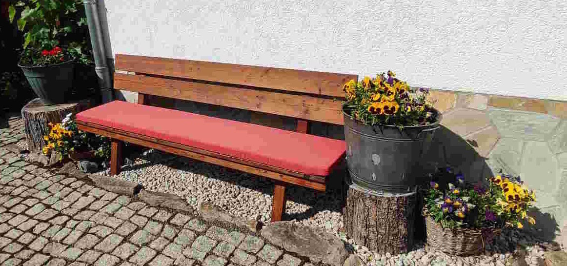 große Bank mit rotem Sitzkissen, an Haus stehend