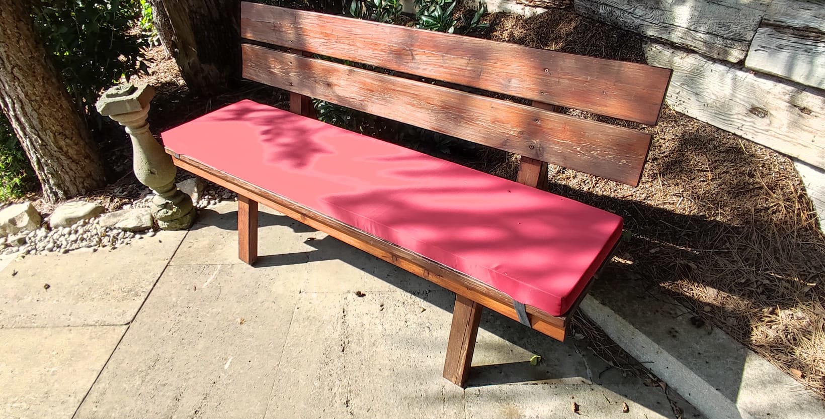 mittlere Bank mit rotem Sitzkissen, an Haus stehend